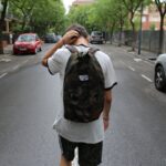 Αγόρι που φοράει λευκό μπλουζάκι και μαύρο σορτς και κουβαλάει σχολικό σακίδιο επιστρέφοντας από το σχολείο