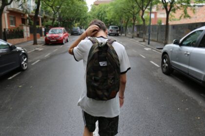 Αγόρι που φοράει λευκό μπλουζάκι και μαύρο σορτς και κουβαλάει σχολικό σακίδιο επιστρέφοντας από το σχολείο