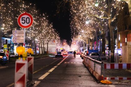 Visitors walk through a German Christmas market in the evening, with festive lights, crowded stalls and visible security presence.