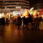A mulled wine stand at a German Christmas market with warm lights and visitors ordering drinks.
